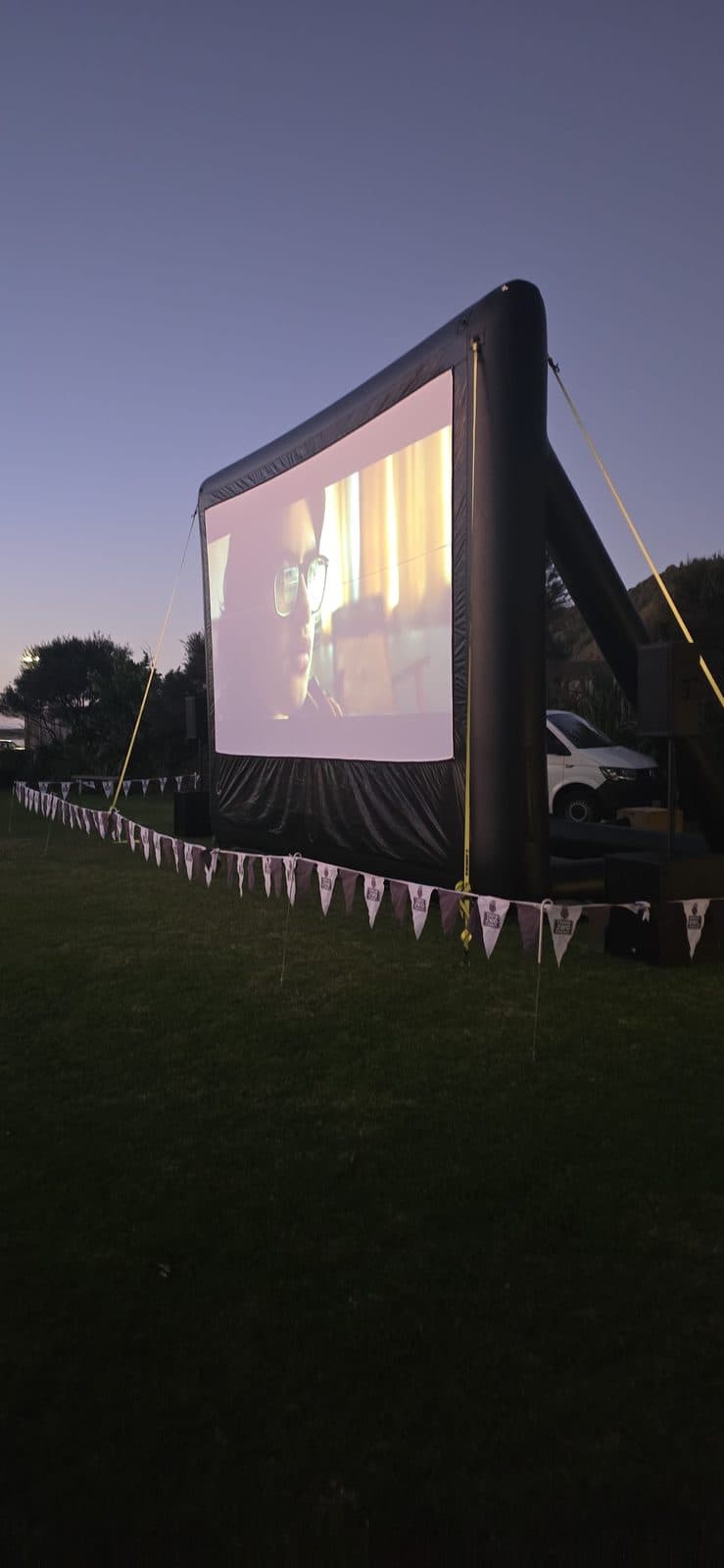 A private outdoor cinema screen glowing at dusk in a backyard setting