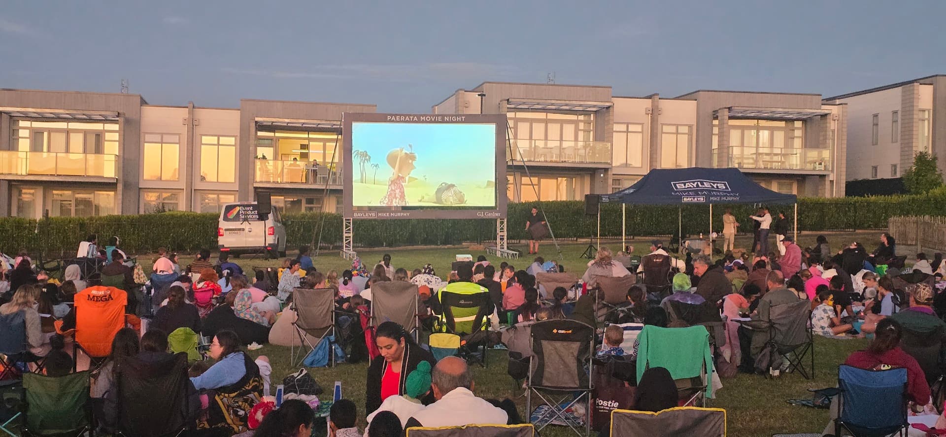 Community gathered on a field watching an outdoor movie at dusk