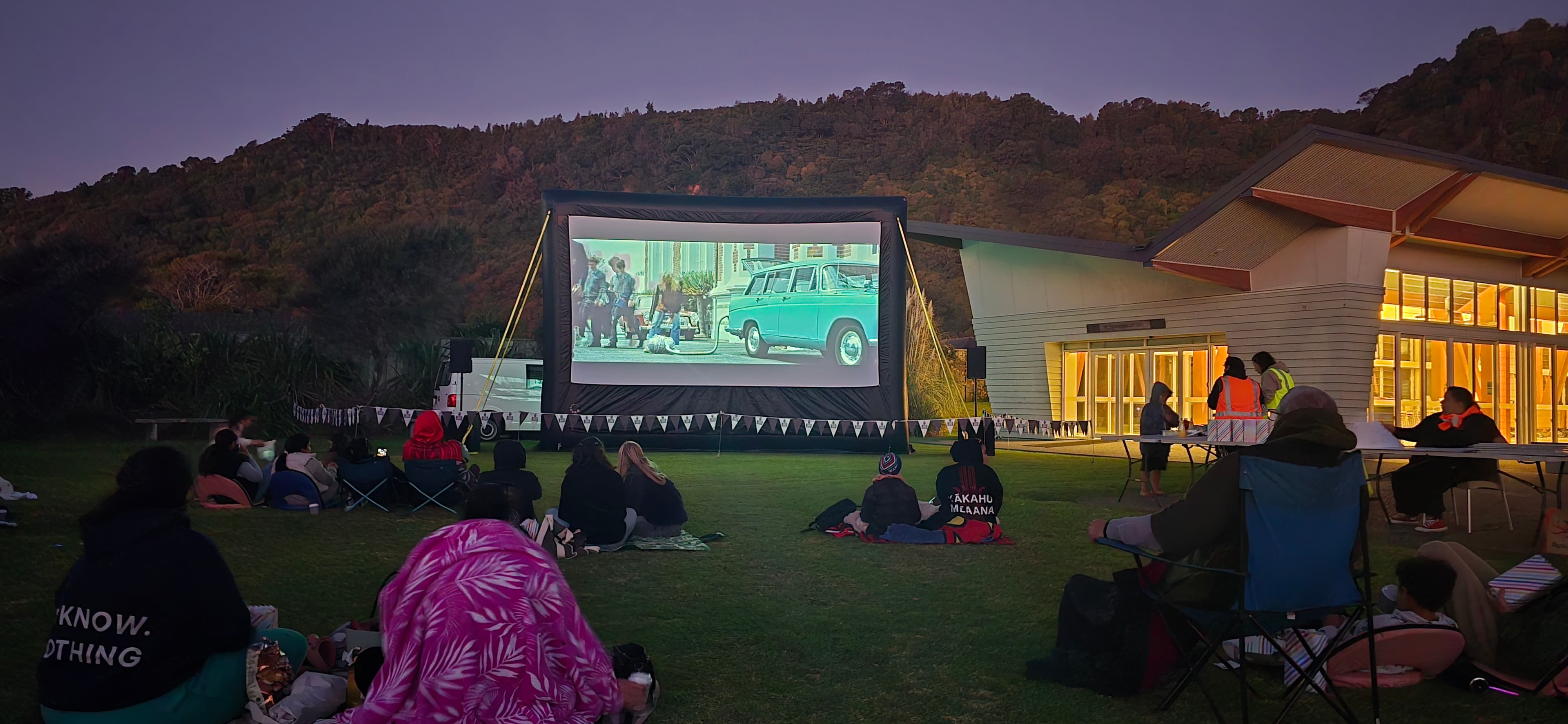 A large crowd gathered on a field at dusk for an outdoor community movie night